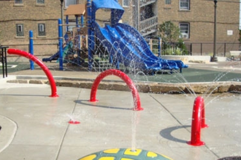 Splash pad with the playground behind it at Lucy Parsons Park.