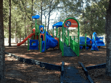 Inclusive playground under shade trees at Roger Scott Athletic Complex in Pensacola