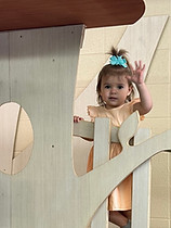 Toddler peeking out from a wooden indoor play structure at Backyard Playroom