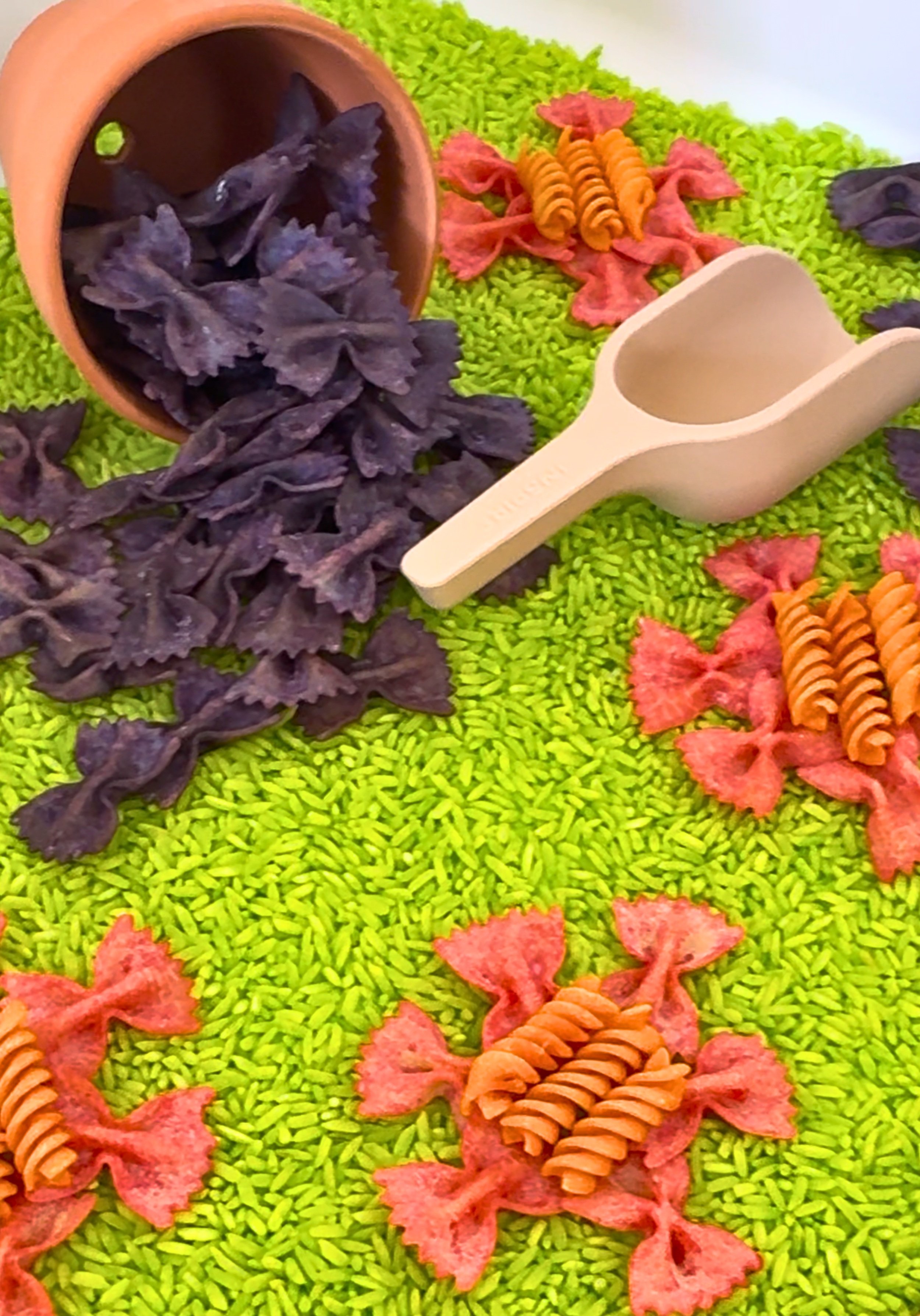 Bright sensory bin with dyed rice, pasta shapes, and scooping tools at Blossom Play Space.