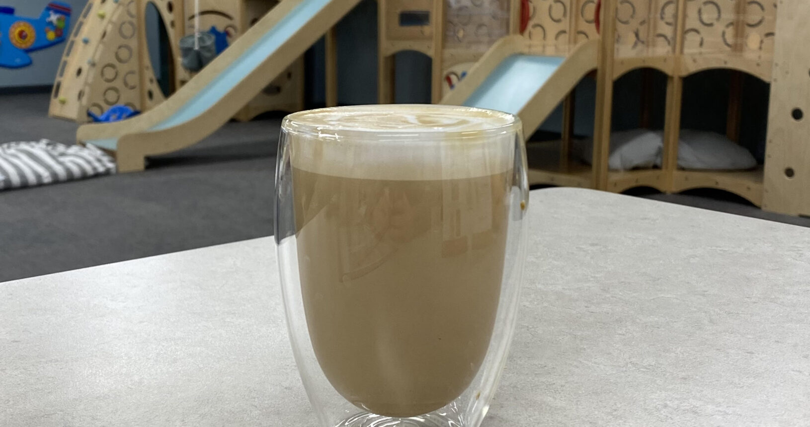 Coffee on a café table with Bug & Goose play structures visible behind it.