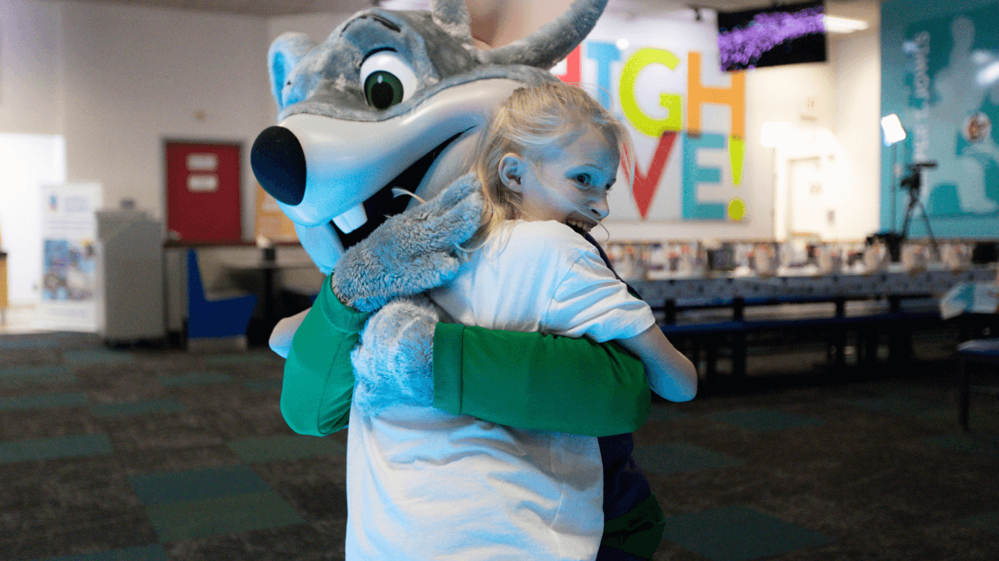 Child hugging Chuck E. Cheese in a quieter dining setting.