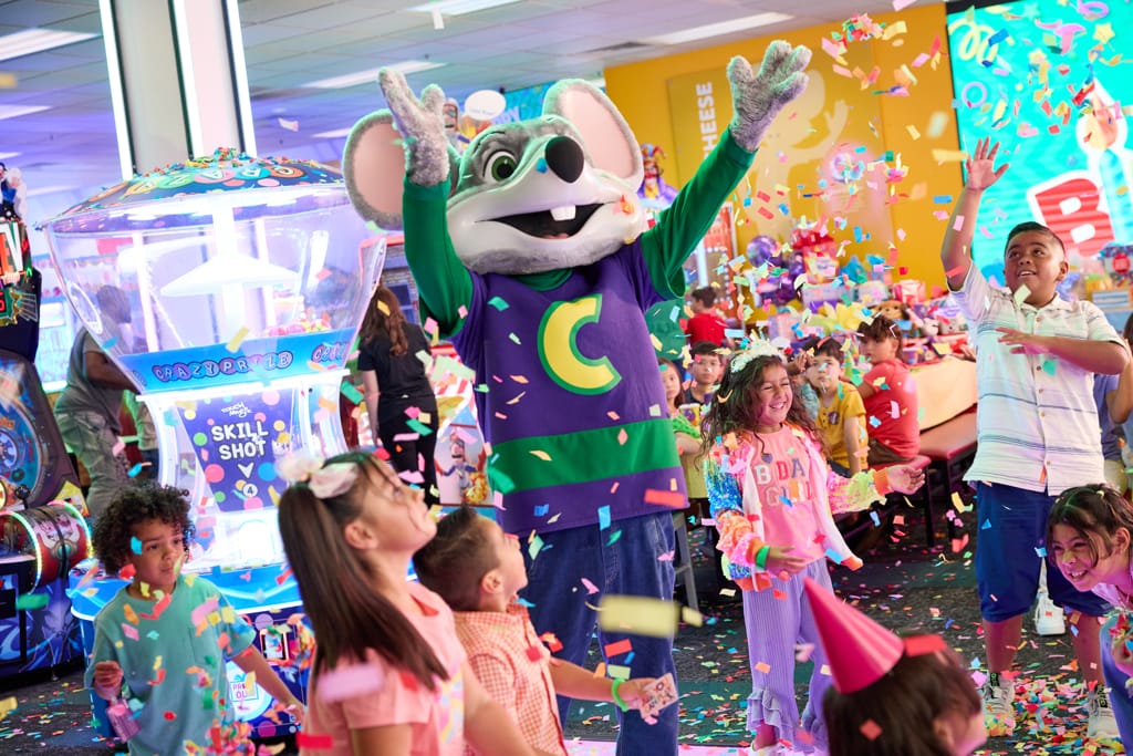 Kids dancing with Chuck E. Cheese during a birthday celebration.
