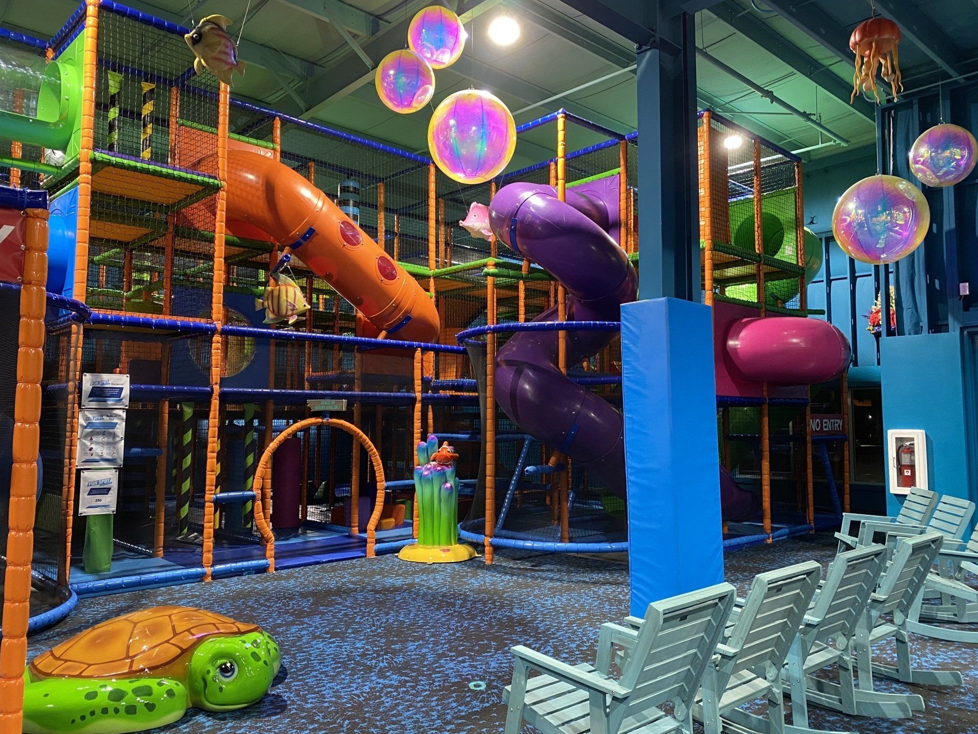 Multilevel indoor playground with bright tube slides and seating at Deep Blue Indoor Play.