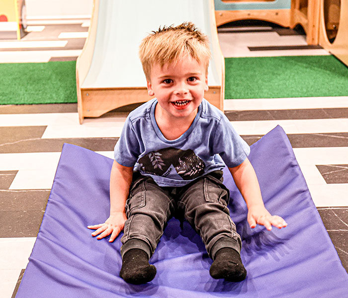 Young child sitting near a small slide in the play café at Electric Donuts.