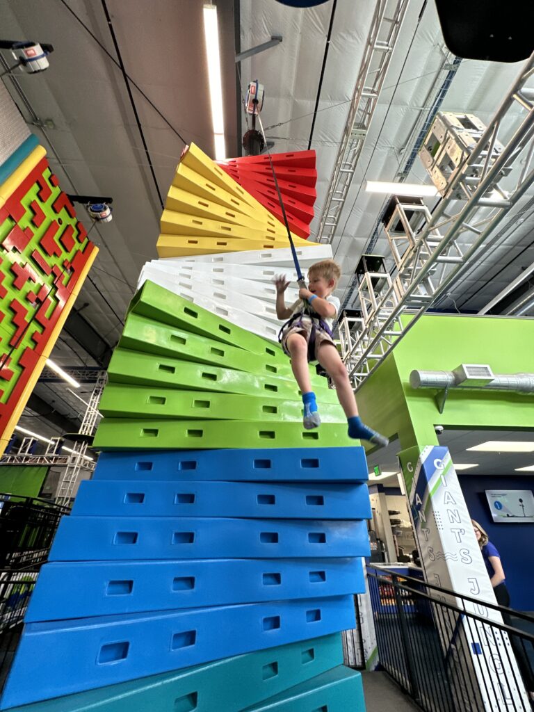 Child climbing a bright geometric wall inside Flying Giant Adventure Park.