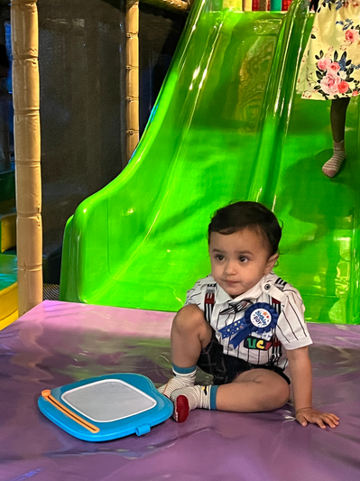 Toddler sitting at the base of a bright green slide at Funzy Play Newport.