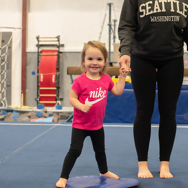 Young child with caregiver on the gym floor during Garland's Gymnastics open gym.