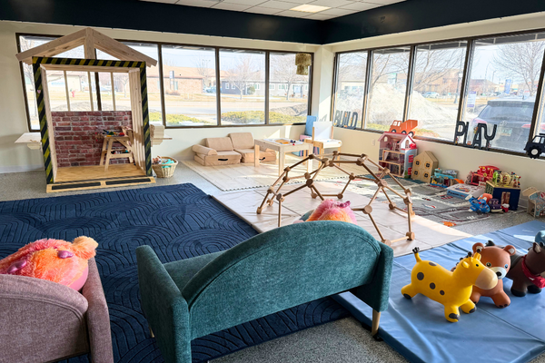 Wide view of Gathered FM's indoor play space with lounge seating, a small playhouse, and toddler-friendly toys.