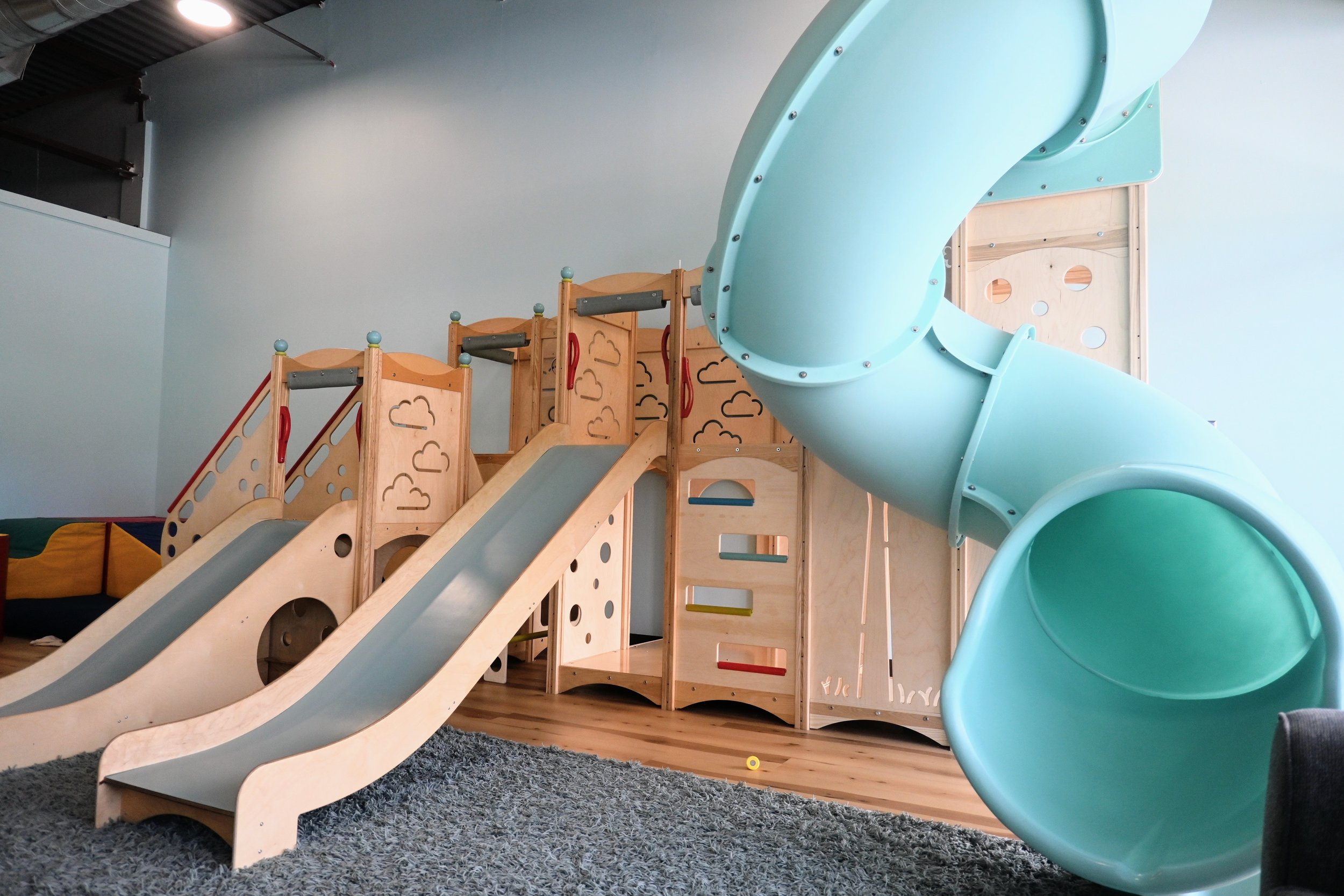 Wide view of the wooden climbing structure and tube slide inside GentleHands.