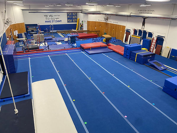 Gold Medal Gymnastics equipment area with spring floor, bars, mats, and foam pit.