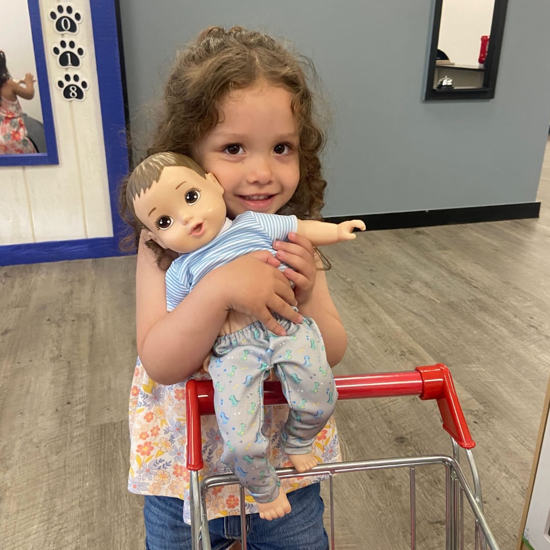 Child holding a doll near a pretend-play station at Goose & Rev Play Co. in Ellensburg.
