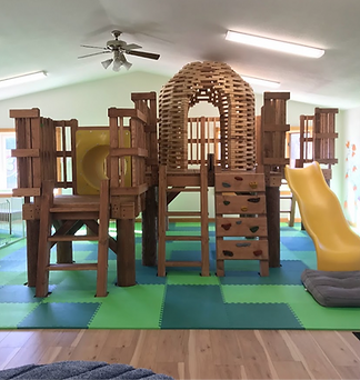 Wooden play structure with tunnel slide and foam mats at Happy Hive.
