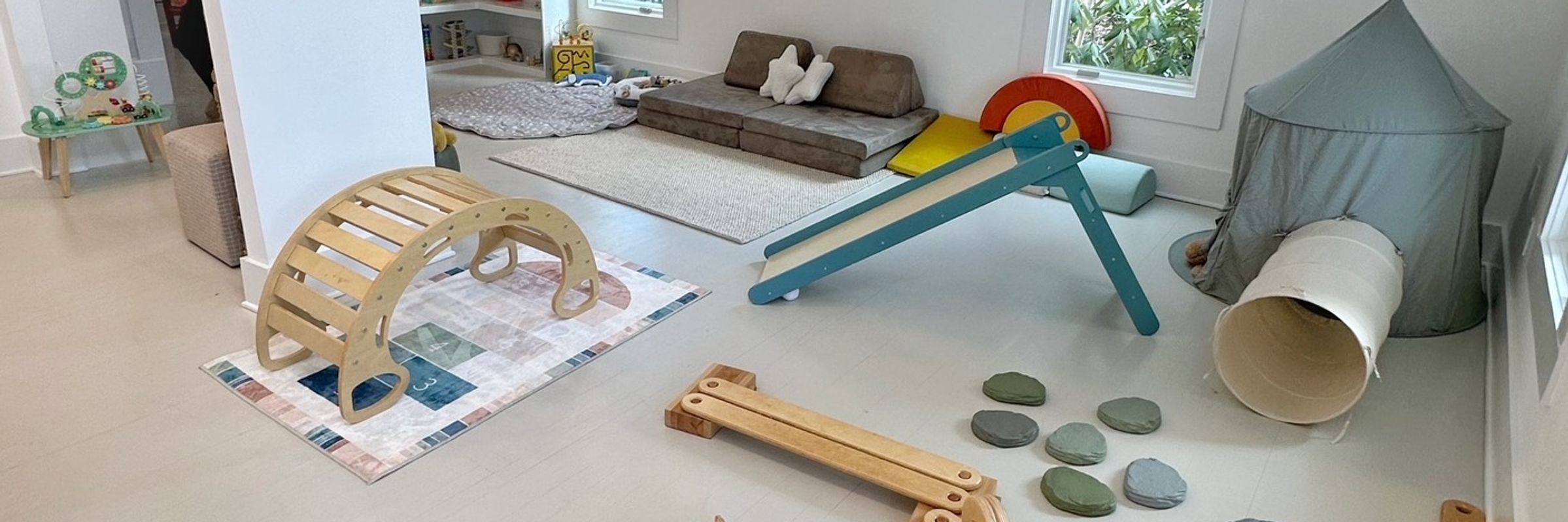 Toddler-friendly playroom with Pikler-style equipment, a slide, and a play tent at Ivy House Play Space.
