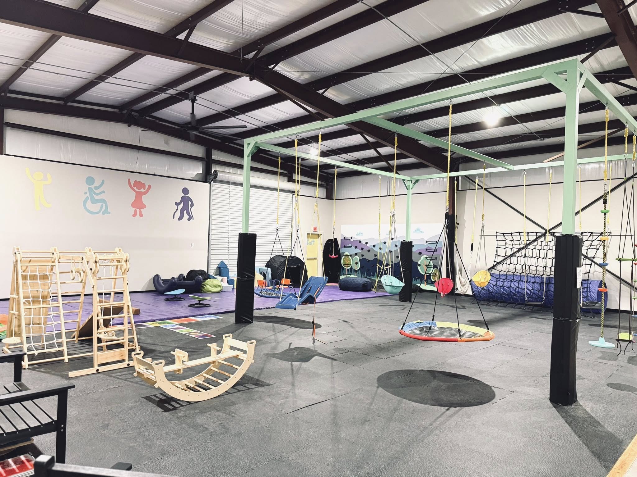 Wide view of the sensory gym floor with swings and climbing equipment.