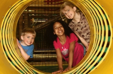 Children smiling inside a tunnel opening on the Jungle Java play structure.