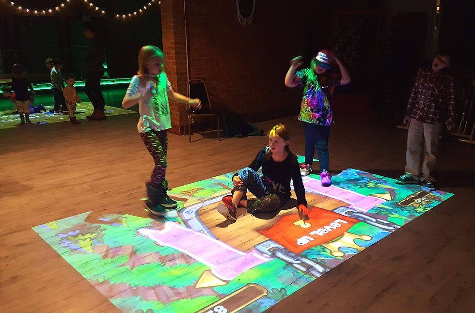 Children playing a projected floor game in a dim indoor studio.