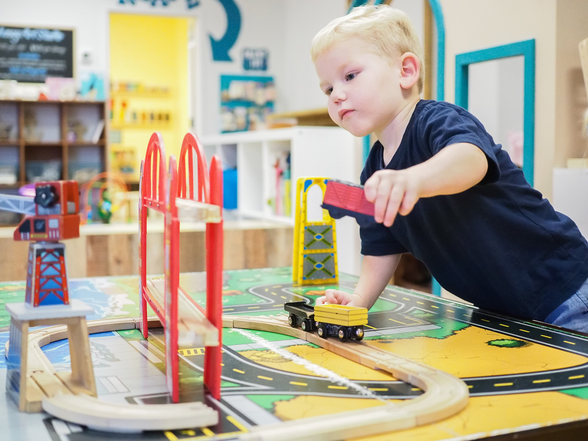 Child playing at a train table inside Little Doodles Play Cafe in Wendell.