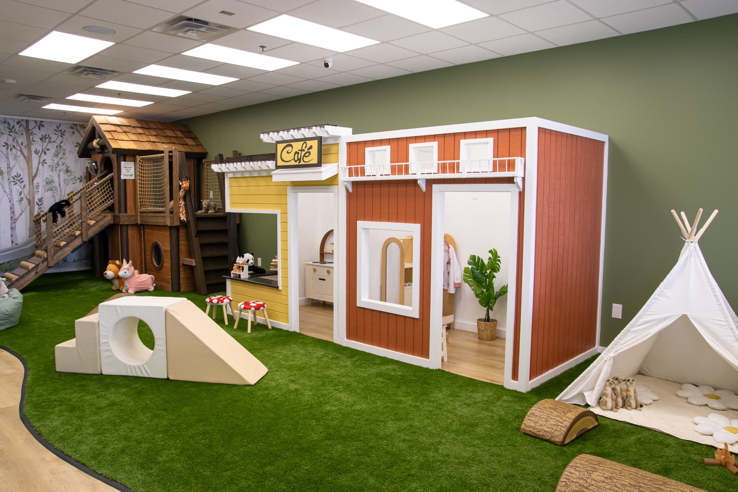 Indoor play village at Little Leaps with a wooden treehouse, pretend café, play house, and teepee.