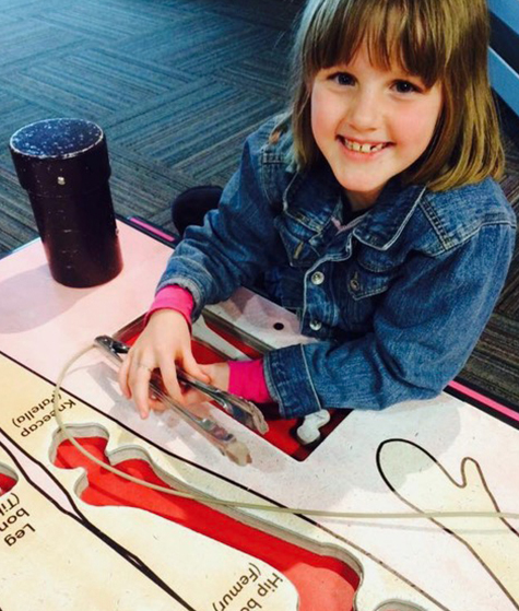 Child smiling while using an interactive tabletop exhibit at the museum.