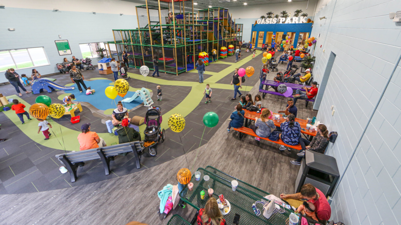Wide view of Oasis Park's indoor play structure and open floor area.