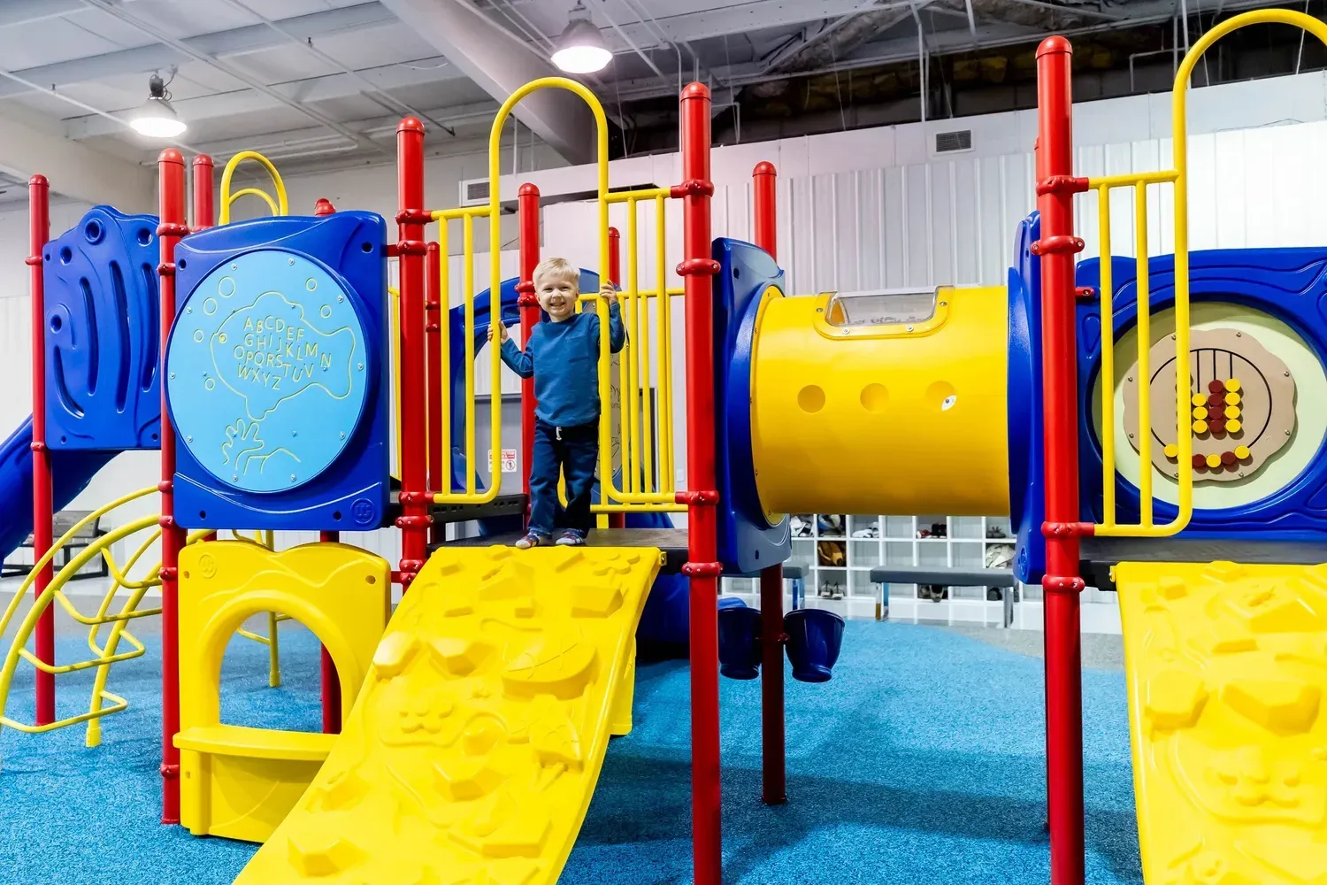 Child standing on a bright yellow-and-blue indoor climbing structure at Play Grounds of La Crosse.