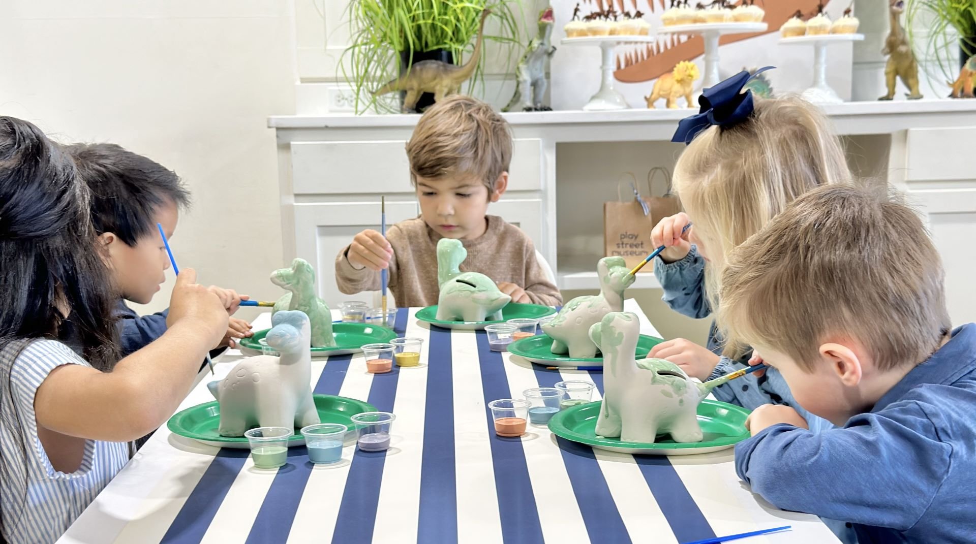 Kids painting dinosaur pottery at Play Street Museum