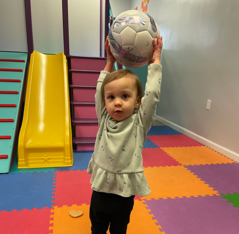 Toddler standing in the mat play area near a small slide at Polkadot Play