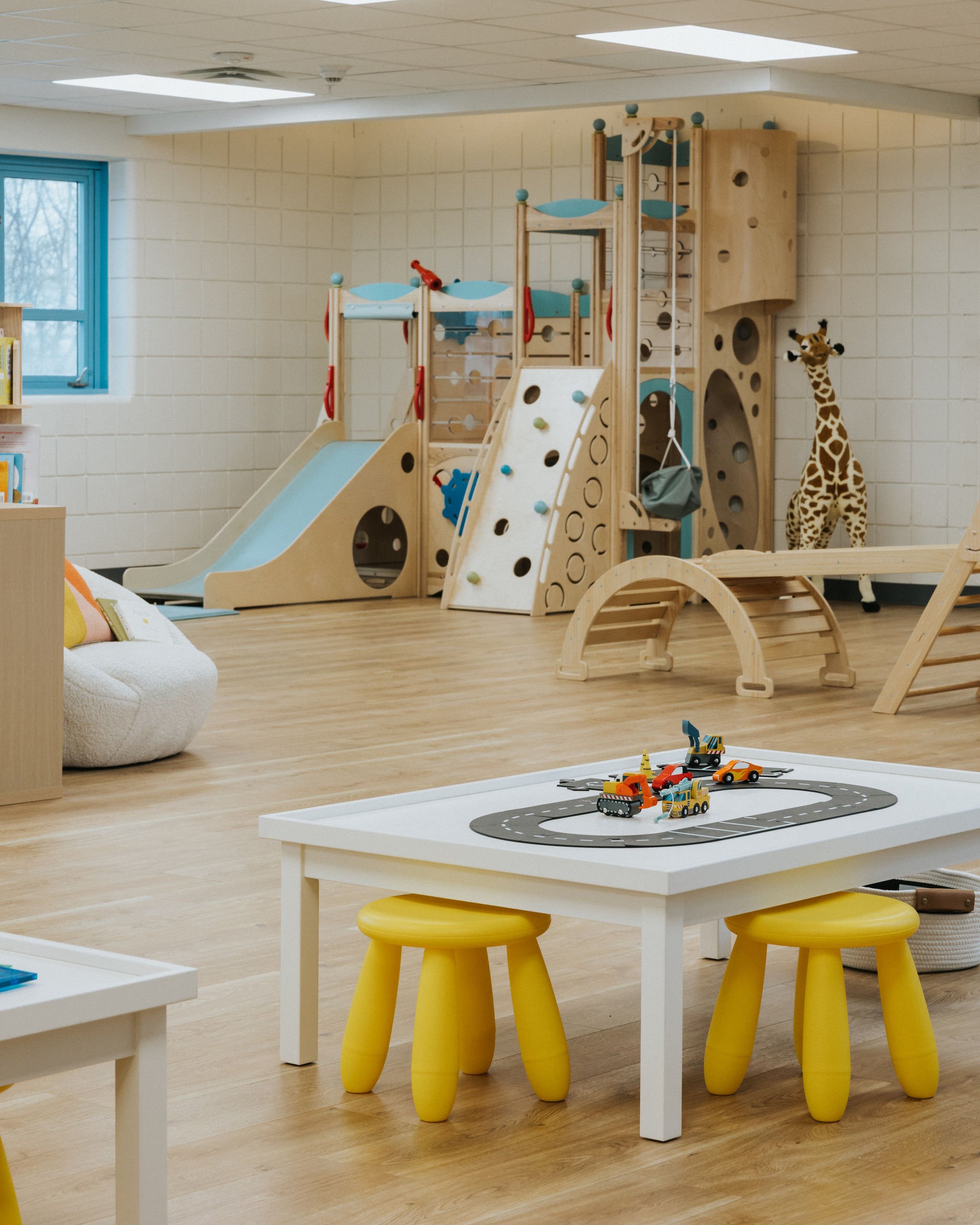 Wide view of Raise Playspace with wooden climber and open toddler play area.