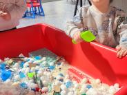 Young child scooping materials at a red sensory table inside Recreation Station.