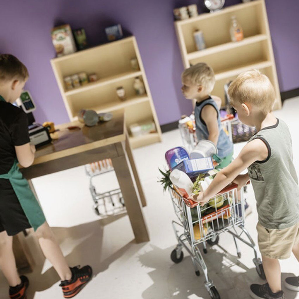 Children exploring pretend-play market shelves at Rise Play Park.