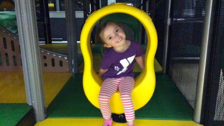 Child sitting in a yellow tunnel opening inside the indoor playground