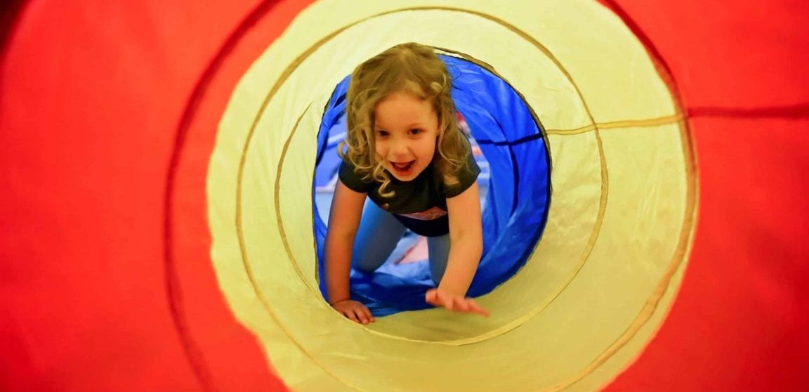 Young child in a tunnel attraction used to illustrate Sky Zone toddler play