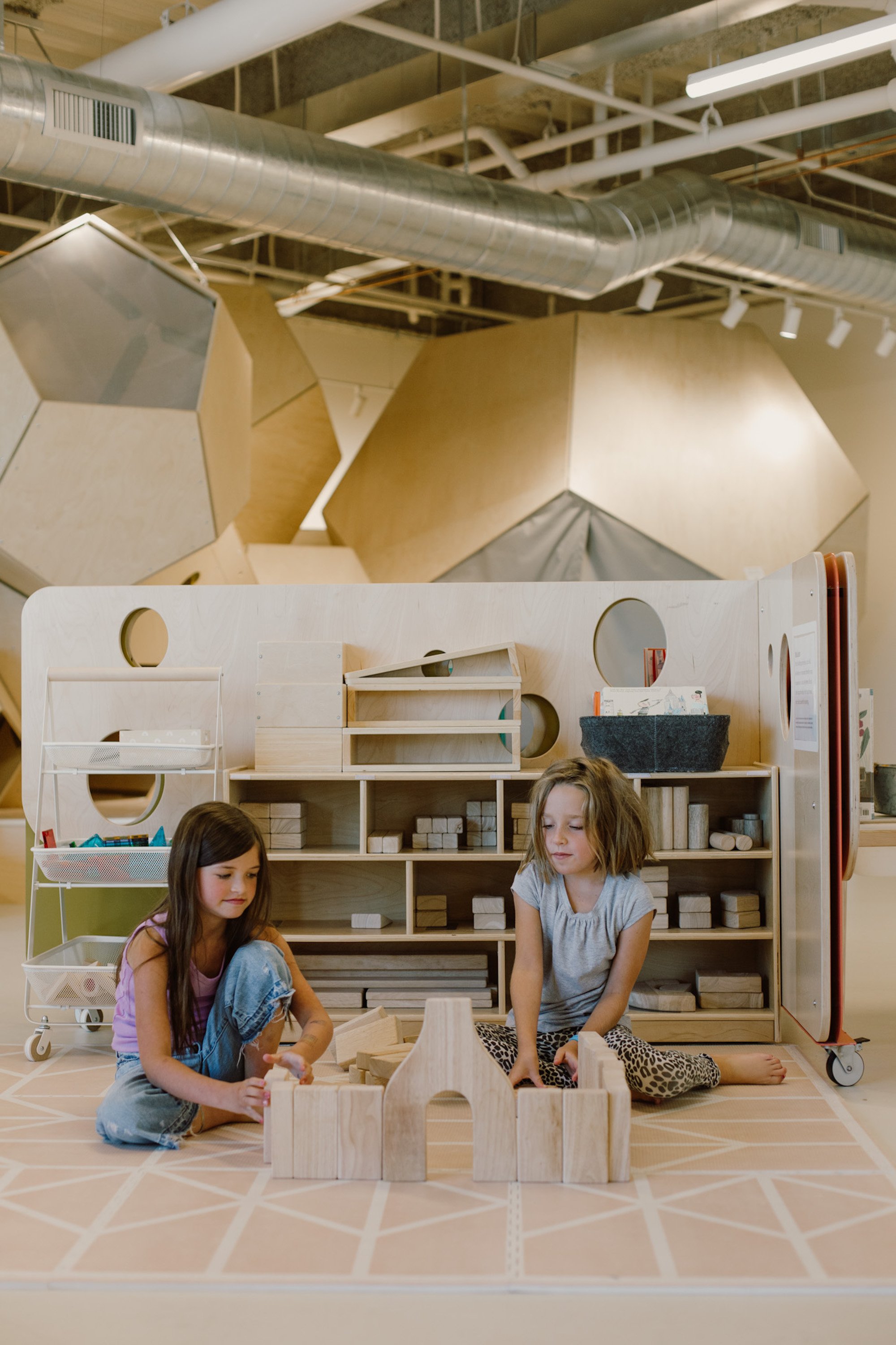 Children playing with wooden blocks beneath the geometric play fort at State of Play in Bozeman