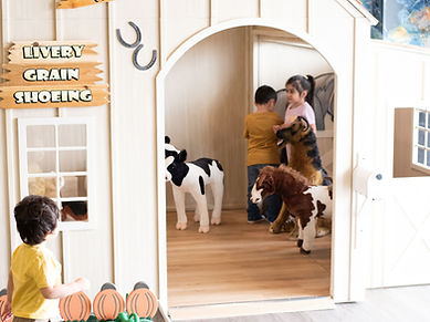 Children playing in a barn-style pretend-play room at The Barnyard Indoor Playground.