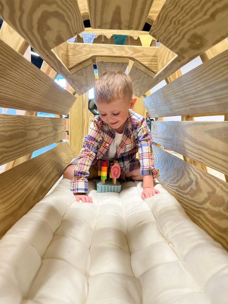 Child climbing through a wooden play structure at The Little Things Play Cafe.