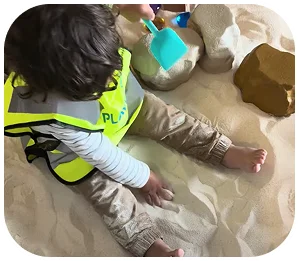 Child seated at the sand play area inside The Sandbox for Kids.