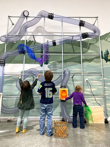 Children playing at the tall tube-wall STEM exhibit at Valley Play Museum.