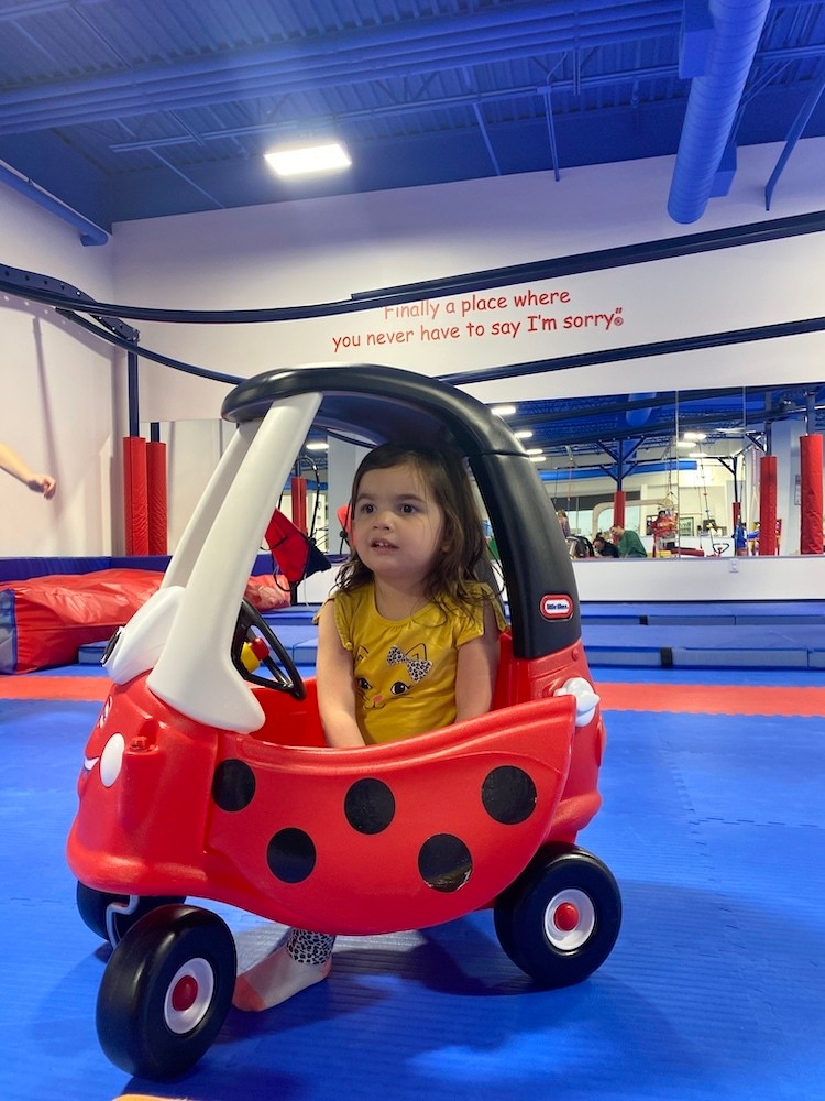 Toddler in ride-on toy inside the padded play gym at We Rock the Spectrum Enid.
