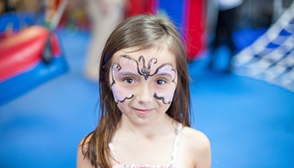 Child in the gym space with bright blue flooring and play equipment in the background.