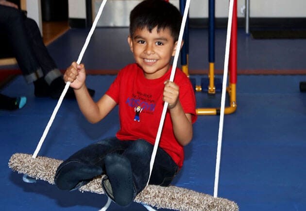 Child sitting on an indoor swing inside the gym.
