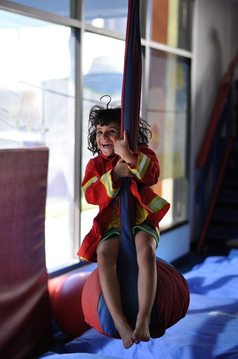 Child smiling while riding a suspended sensory swing at We Rock the Spectrum Yukon