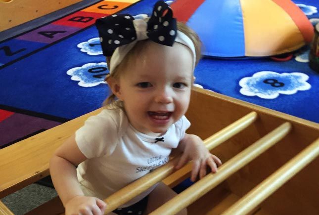 Toddler smiling while climbing into a wooden rocker at Whiz Kids Naples.