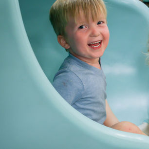 Child smiling inside a slide tube at Wild Child Indoor Playground.