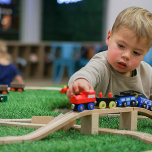 Child pushing toy trains along a small track at Wild Child Indoor Playground.