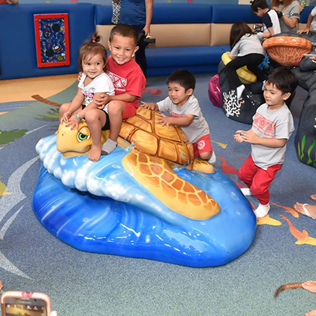Children playing on the turtle sculpture at the Windward Mall Play Area.