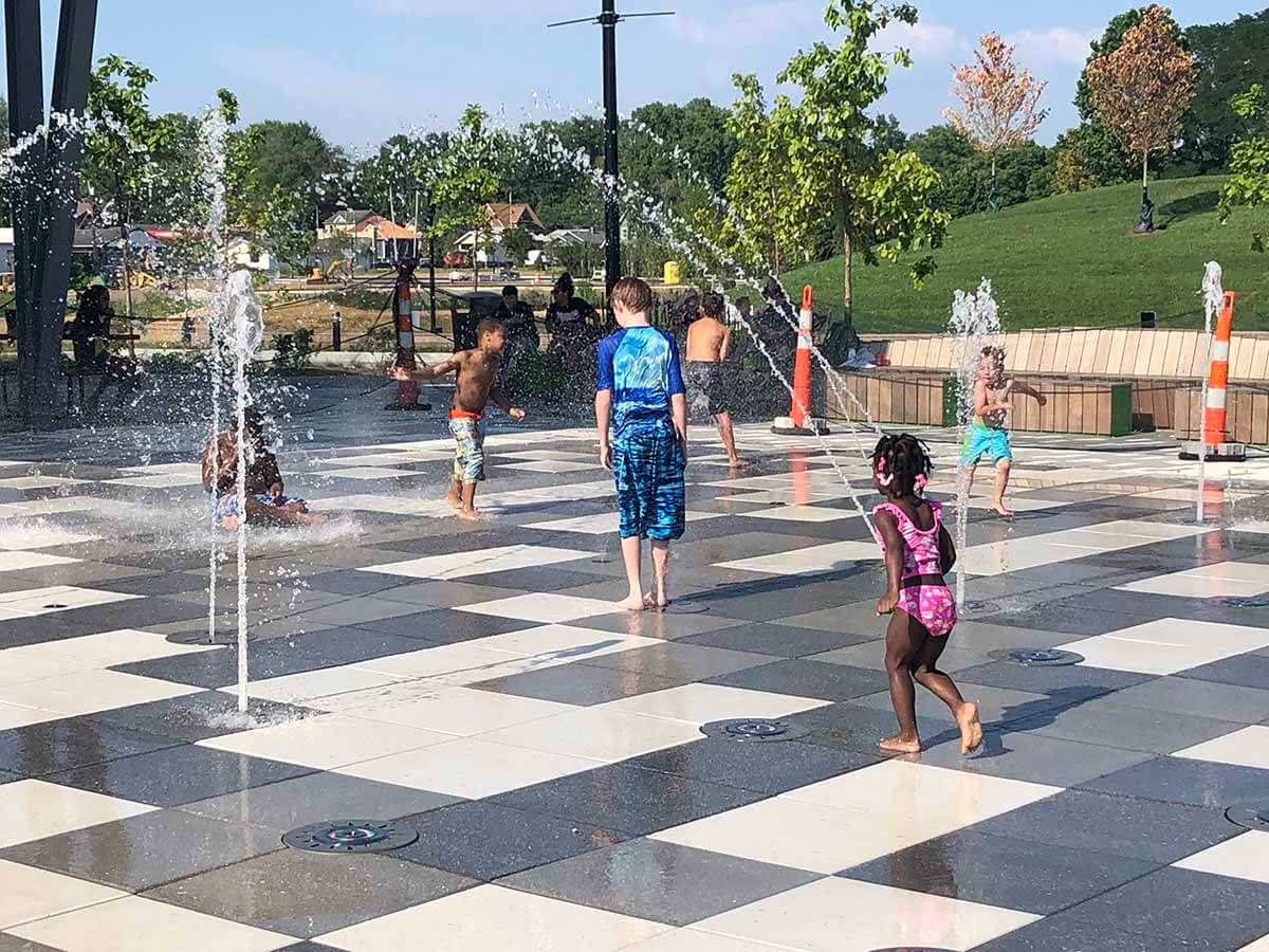 Children running between water jets at the Community Foundation Switchyard Plaza Spray Pad.