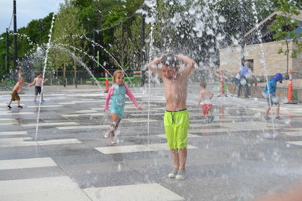 A vibrant community spray pad with water jets and kids playing on a sunny day.
