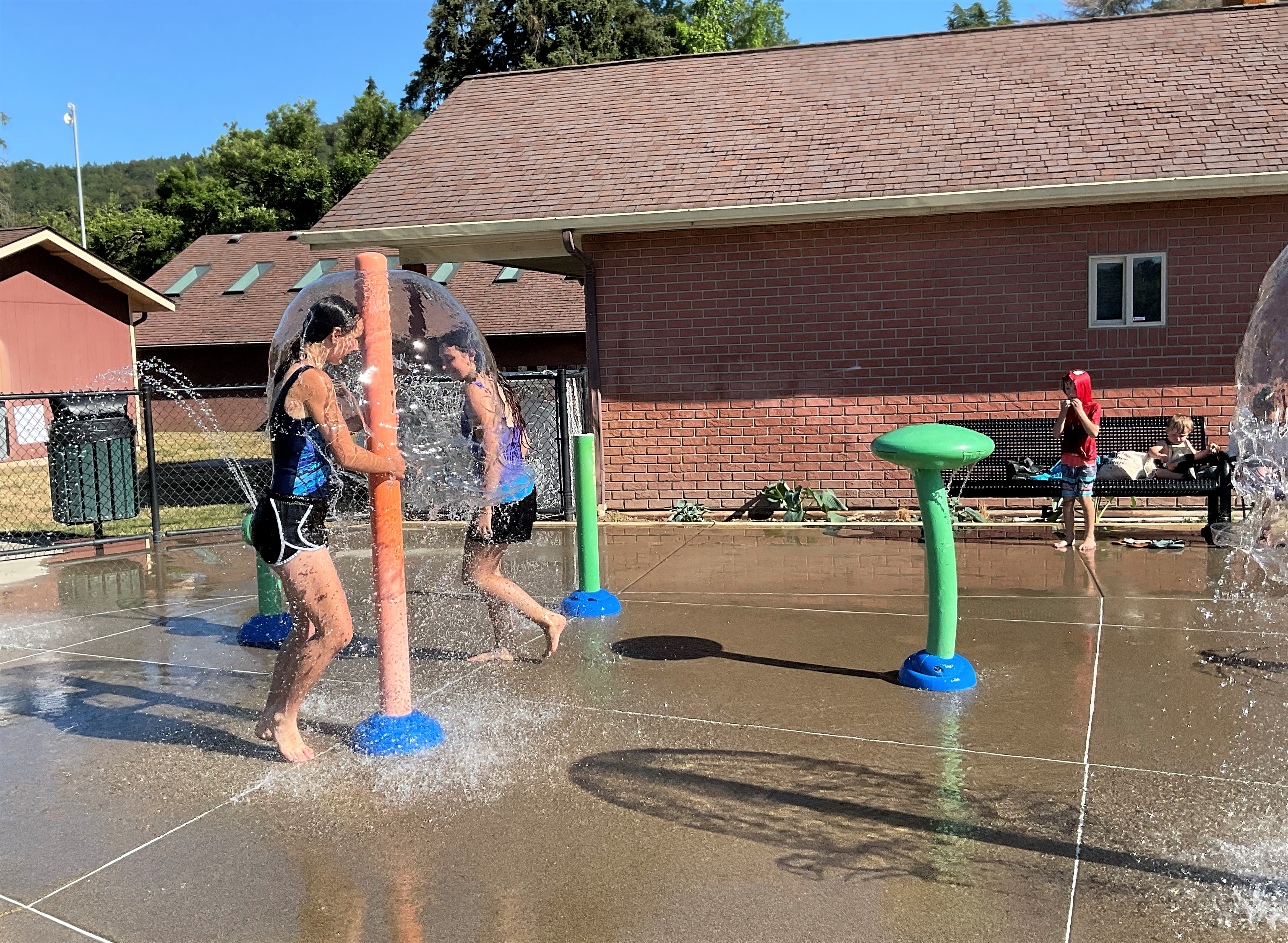 Kids playing beneath an umbrella-style water feature at Fir Grove Park Splash Pad.