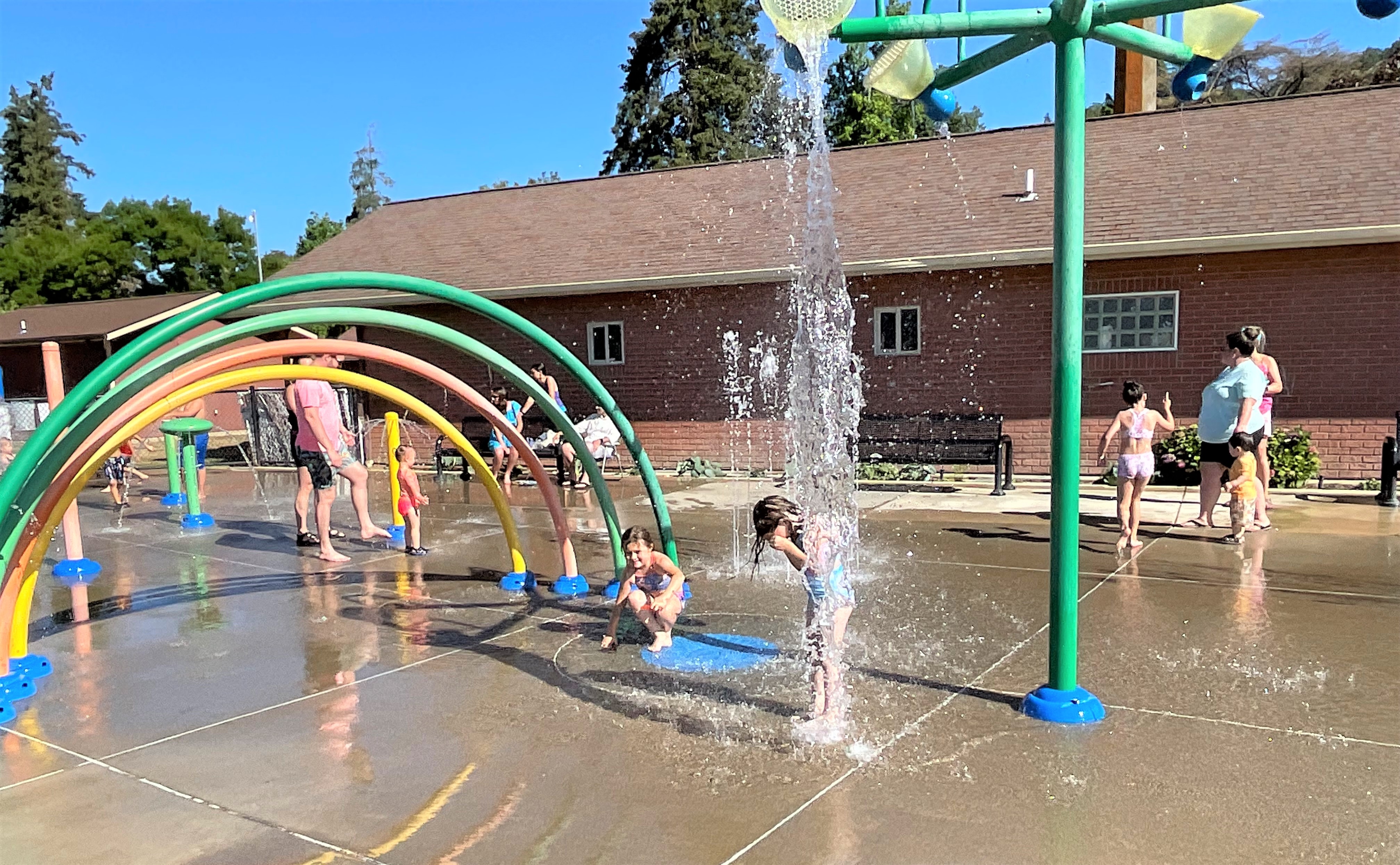 Child getting splashed by a larger water feature at Fir Grove Park Splash Pad.